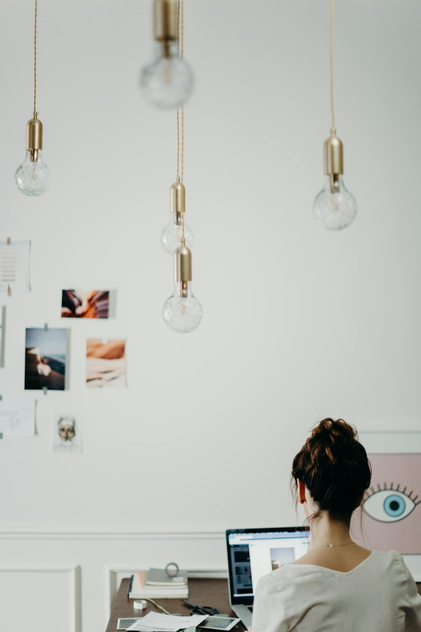 Woman working at a desk in a modern creative office, surrounded by mood boards and hanging lightbulbs.